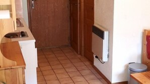 A room with a wooden door, a radiator, a trash bin, and a small table. - Cosy 2-Room Mezzanine Apartment, Sleeps 5, South-Facing Balcony, Near Linga Lift, Parking Included (Châtel)