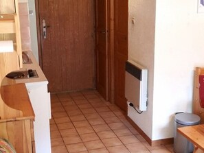 A room with a wooden door, a radiator, a trash bin, and a small table. - Cosy 2-Room Mezzanine Apartment, Sleeps 5, South-Facing Balcony, Near Linga Lift, Parking Included (Châtel)