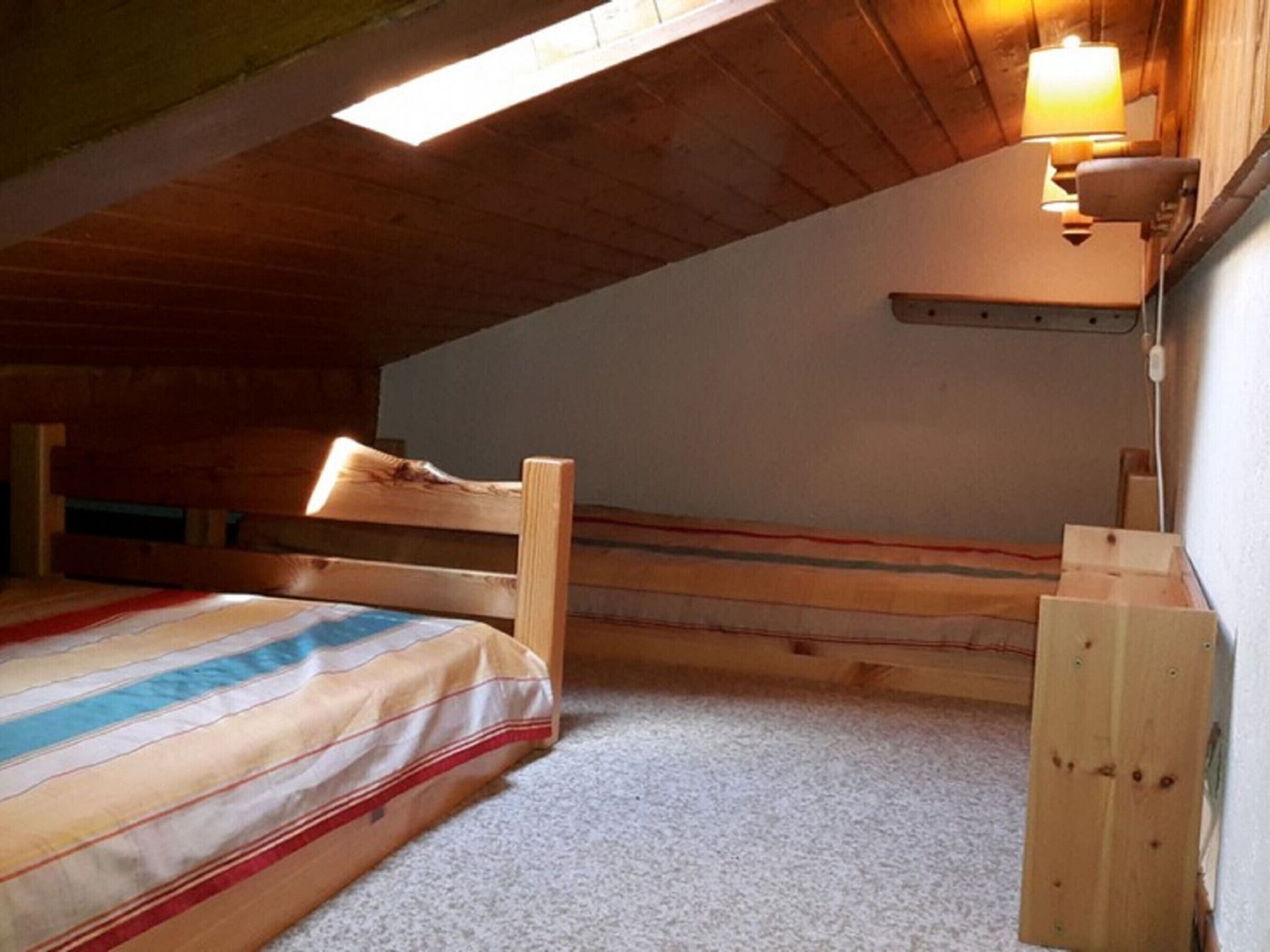 A small, cozy attic bedroom with a sloped ceiling, a single bed, a nightstand, and a wall-mounted lamp.