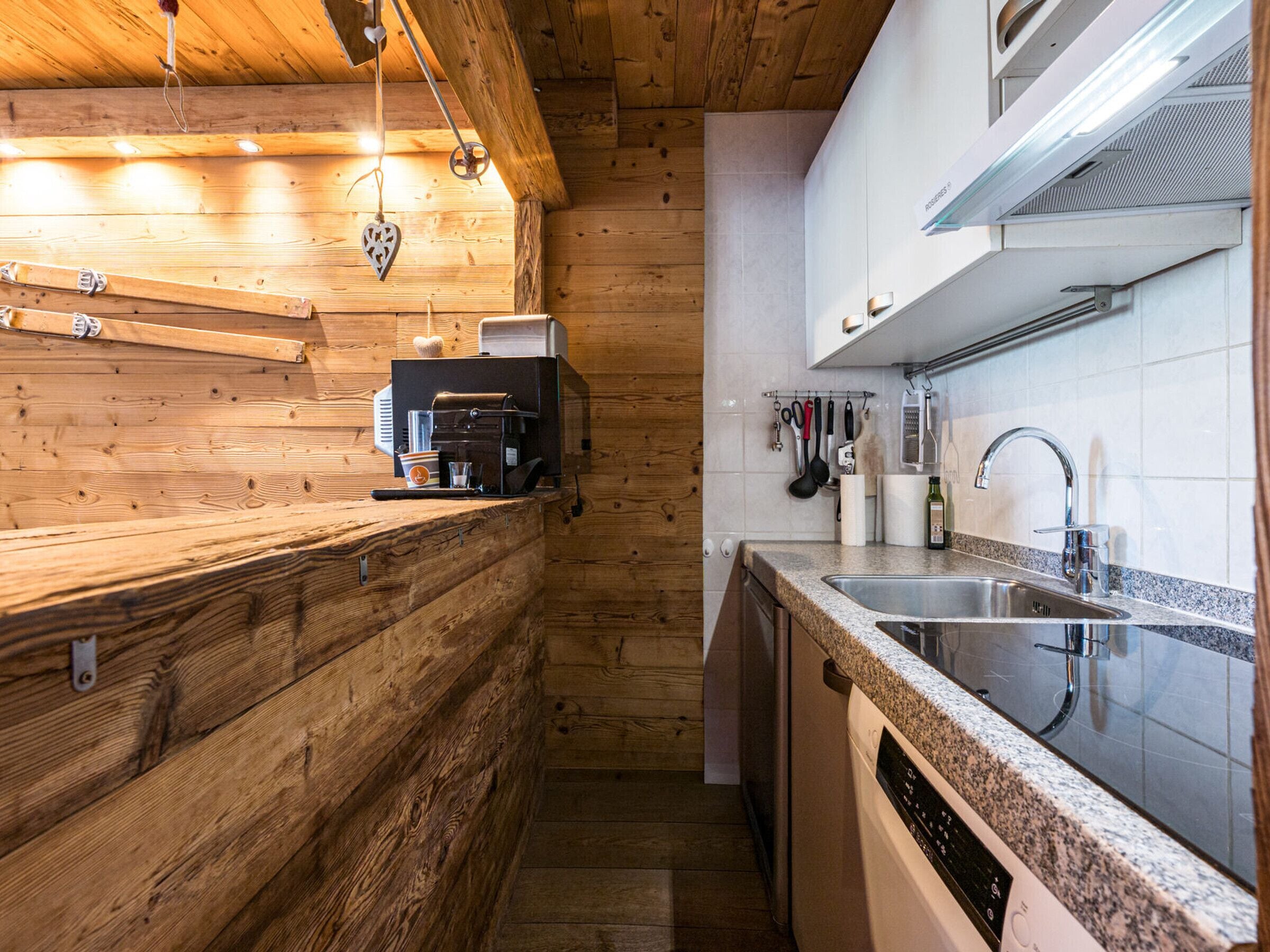 A kitchen with wooden walls, a coffee machine, and a stainless steel sink.