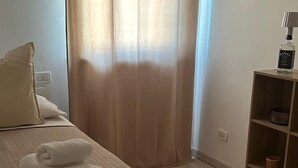 Una habitación de hotel con cama, repisas con artículos de aseo y una ventana con cortinas.