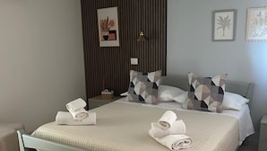 Una cama bien tendida con toallas, una lámpara de noche y una pared con líneas verticales y obras de arte enmarcadas.