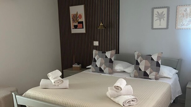 Una cama bien tendida con toallas, una lámpara de noche y una pared con líneas verticales y obras de arte enmarcadas.