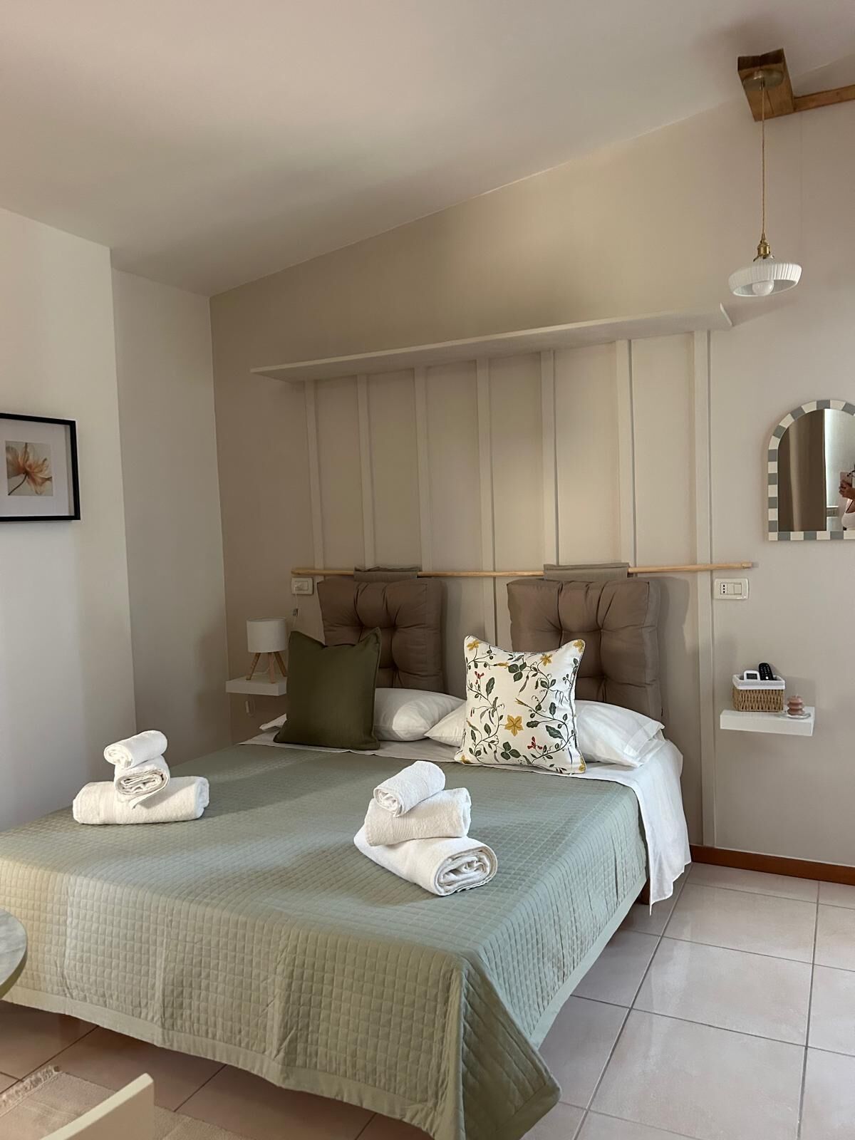 Une chambre d’hôtel avec un lit, deux oreillers, une table de chevet, un miroir et une serviette sur le lit.