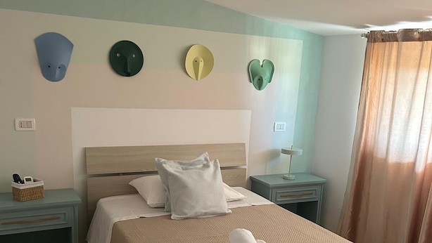 Una habitación de hotel con cama, dos mesitas de noche, una lámpara de pared y una cortina.