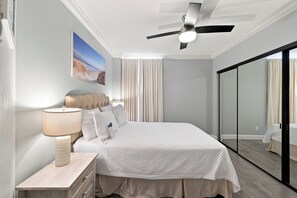 Ein Hotelzimmer mit Bett, Nachttisch, Lampe, Deckenventilator, einem Bild an der Wand und einer Schiebeglasdoor.