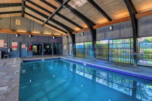 An indoor swimming pool with a wooden ceiling, tiled floor, and a view of a fenced outdoor area. - Windward Pointe 1204 by Liquid Life (Orange Beach)