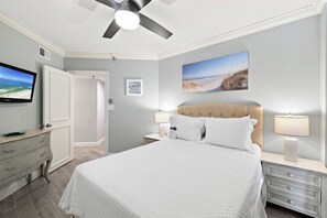 A bedroom with a bed, two bedside tables with lamps, a ceiling fan, a television on the wall, and a painting above the bed. - Windward Pointe 1204 by Liquid Life (Orange Beach)