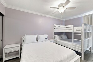 A bedroom with a bunk bed, a single bed, a nightstand, and a ceiling fan. - Windward Pointe 1204 by Liquid Life (Orange Beach)