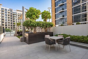 An outdoor patio area with a table and chairs, surrounded by greenery and modern buildings. - Free Housekeeping Visits During Your Stay - Stayshort - Luxury Studio Apartment in Meydan With Balcony (Dubai)