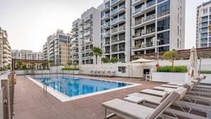 A modern apartment complex with a swimming pool, lounge chairs, and a covered outdoor area. - Free Housekeeping Visits During Your Stay - Stayshort - Luxury Studio Apartment in Meydan With Balcony (Dubai)