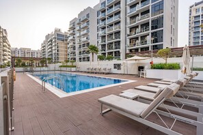 A modern apartment complex with a swimming pool, lounge chairs, and a covered outdoor area. - Free Housekeeping Visits During Your Stay - Stayshort - Luxury Studio Apartment in Meydan With Balcony (Dubai)