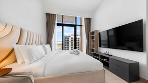 A modern hotel room with a large bed, a flat-screen TV, a wooden side table, and a view of the cityscape. - Free Housekeeping Visits During Your Stay - Stayshort - Luxury Studio Apartment in Meydan With Balcony (Dubai)
