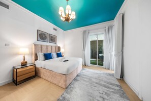 Ein Schlafzimmer mit Bett, Nachttischen, einer Kristallleuchtre und Blick ins Freie.