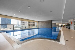 Ein Hallenbad mit hellblauen Fliesen, einem gefliesten Boden und Blick auf eine Stadtkulisse durch große Fenster.