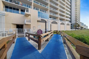 A hotel entrance with a blue mat leading to a wooden deck, a sign for a shower and wash station, and a building with multiple balconies. - San Carlos 1409 by Liquid Life (Gulf Shores)