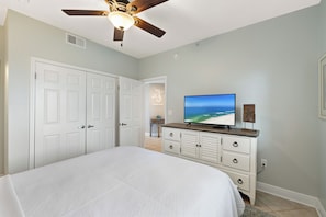 A bedroom with a bed, a ceiling fan, a TV, a dresser, and a door. - San Carlos 1409 by Liquid Life (Gulf Shores)