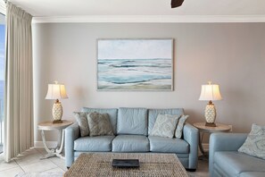 A living room with a light blue sofa, two side tables with lamps, a woven coffee table, and a painting of the ocean on the wall. - San Carlos 1409 by Liquid Life (Gulf Shores)