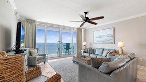Un salon spacieux avec balcon, un ventilateur de plafond, une télévision et un ensemble de canapés.