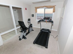 Ein Heimfitnessraum mit Laufband und Ergometer, einer Schiebetür und Blick auf den Ozean.