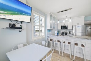 A modern kitchen with white cabinets, a stainless steel refrigerator, and a bar area with white stools. - Royal Palms 1008 by Liquid Life (Gulf Shores)