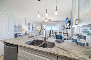A modern kitchen with a marble countertop, double sink, and a dining area with a view of the ocean. - Royal Palms 1008 by Liquid Life (Gulf Shores)
