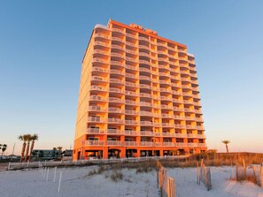 A high-rise hotel with multiple balconies, located near a beach with sand and sparse vegetation. - Royal Palms 1008 by Liquid Life (Gulf Shores)
