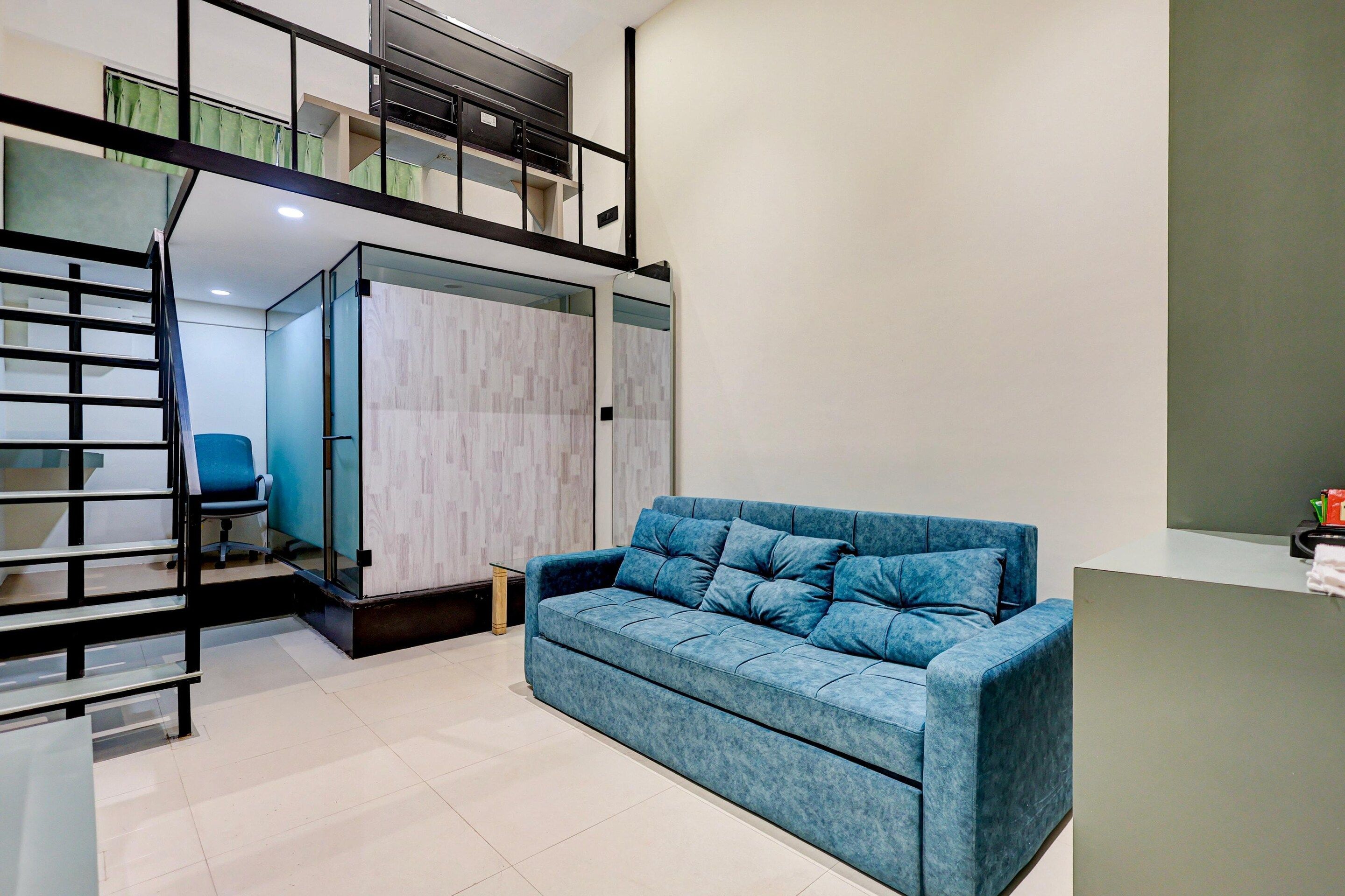 A modern living room with a blue sofa, a glass partition, and a black staircase.
