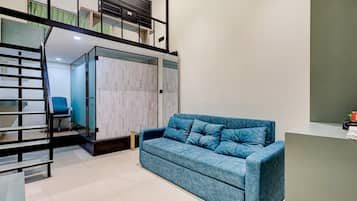 A modern living room with a blue sofa, a glass partition, and a black staircase.