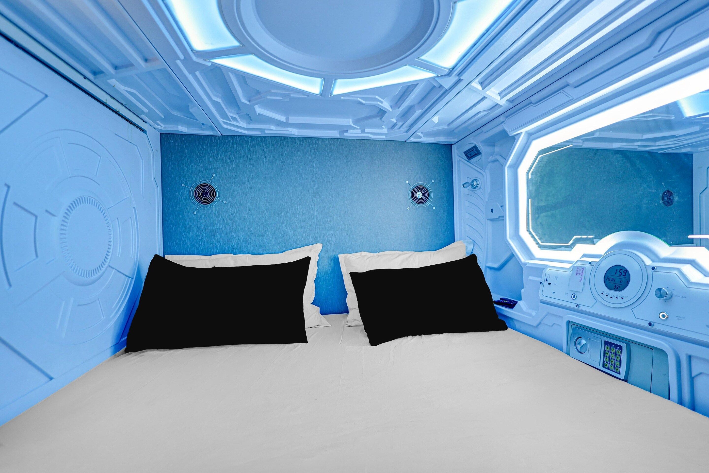 A futuristic room with a bed, control panels, and a window.