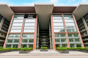 A modern building with a central atrium, large windows, and a sign indicating it is a collection of serviced apartments.
