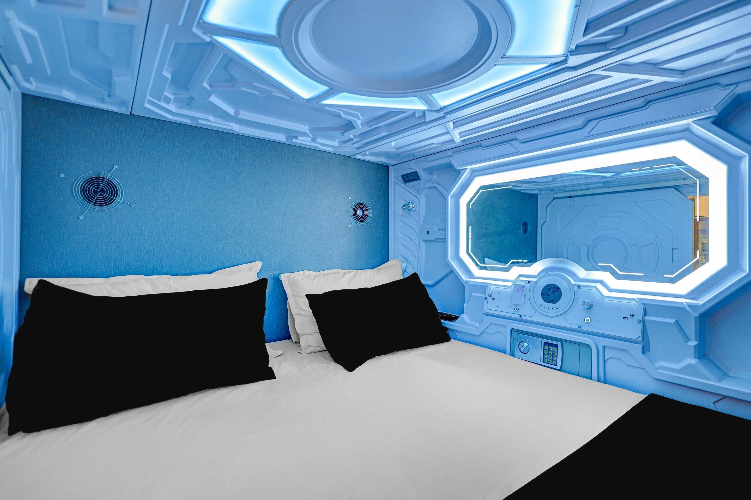 A futuristic room with a bed, a control panel, and a large window.