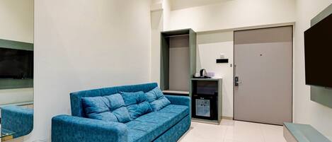 A modern living room with a blue sofa, a glass coffee table, a flat-screen TV, and a door.