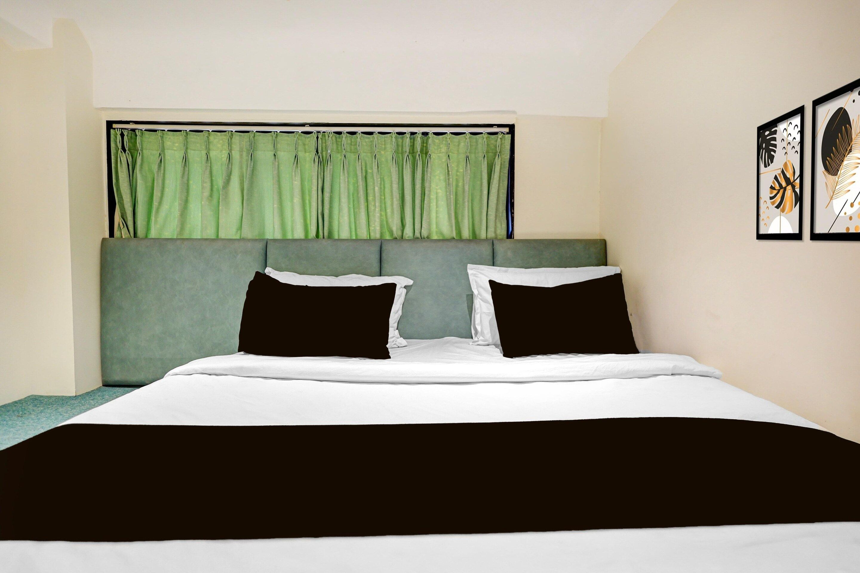 A bedroom with a bed, green curtains, and two framed artworks on the wall.