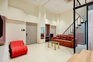 A modern living room with a glass coffee table, a red chair, a brown leather sofa, and a staircase. - Classic Nano Pod (Surat)
