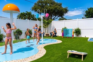 A backyard with a water play area, a white fence, and a wooden bench. - Resort-style 5BR/3BA home, 8 min to Anna Maria Island. Private heated pool, splash pad, home theater, arcade, pickleball court, sauna & hot tub — sleeps 18 with a boat-themed bunk room kids love. Everything your group needs, right at home. (Bradenton)