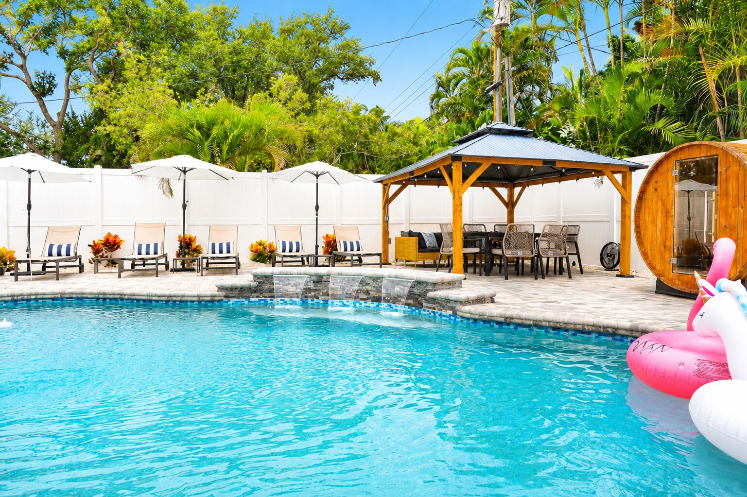 A swimming pool with lounge chairs and umbrellas, surrounded by greenery.