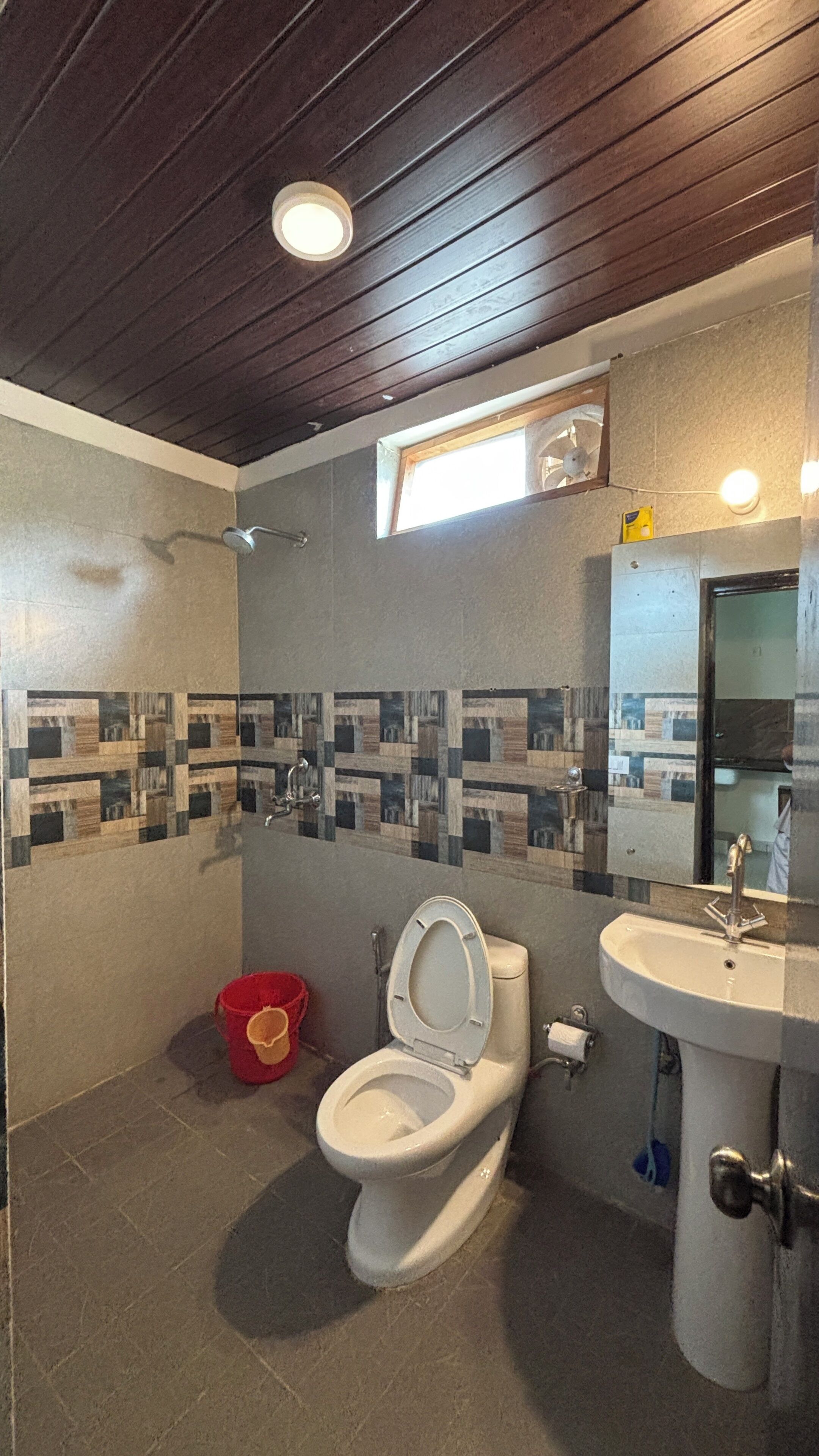 A bathroom with a white toilet, a sink, and a shower. There is a window above the toilet and a mirror above the sink.