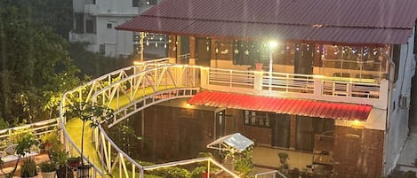 A building with a red roof, a white fence, and a paved area with potted plants.