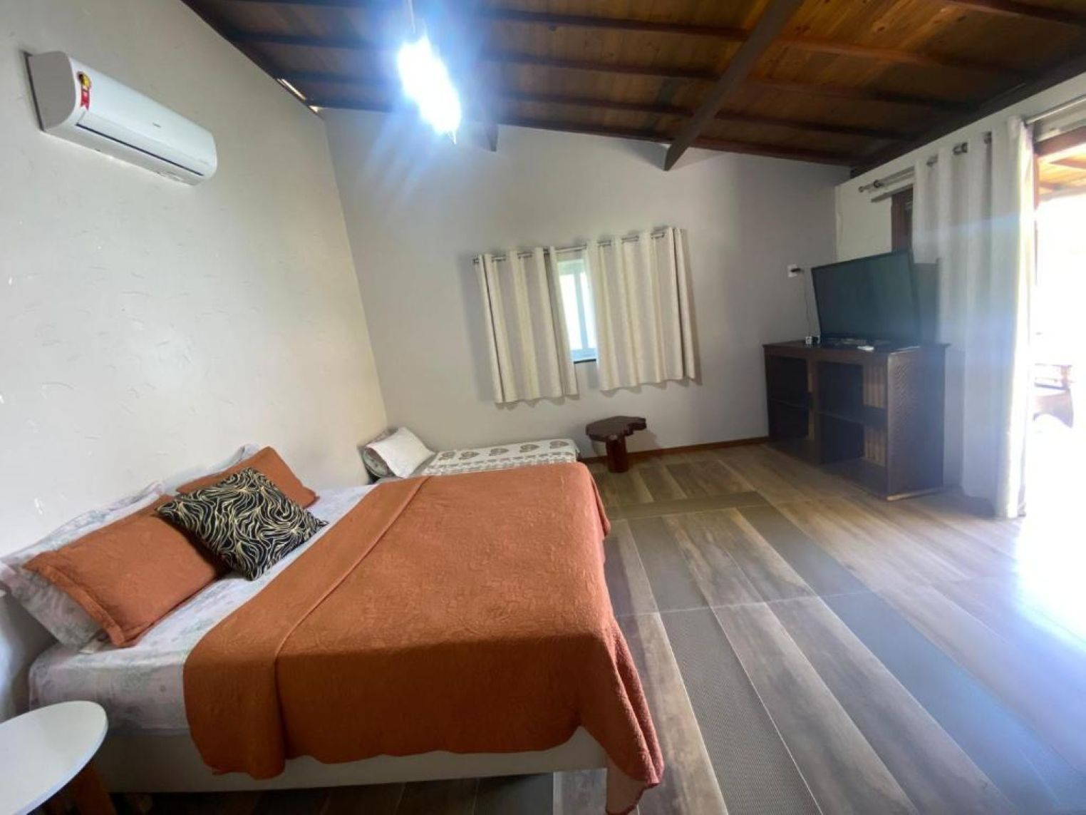 Una habitación con cama, escritorio, televisor y ventana con cortinas.