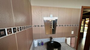 A bathroom with a large mirror, a black sink, and a tiled wall. - Pousada destino  (Entre rios)