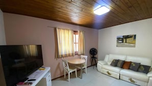 A living room with a television, a white sofa, a dining table with chairs, and a ceiling fan. - Pousada destino  (Entre rios)
