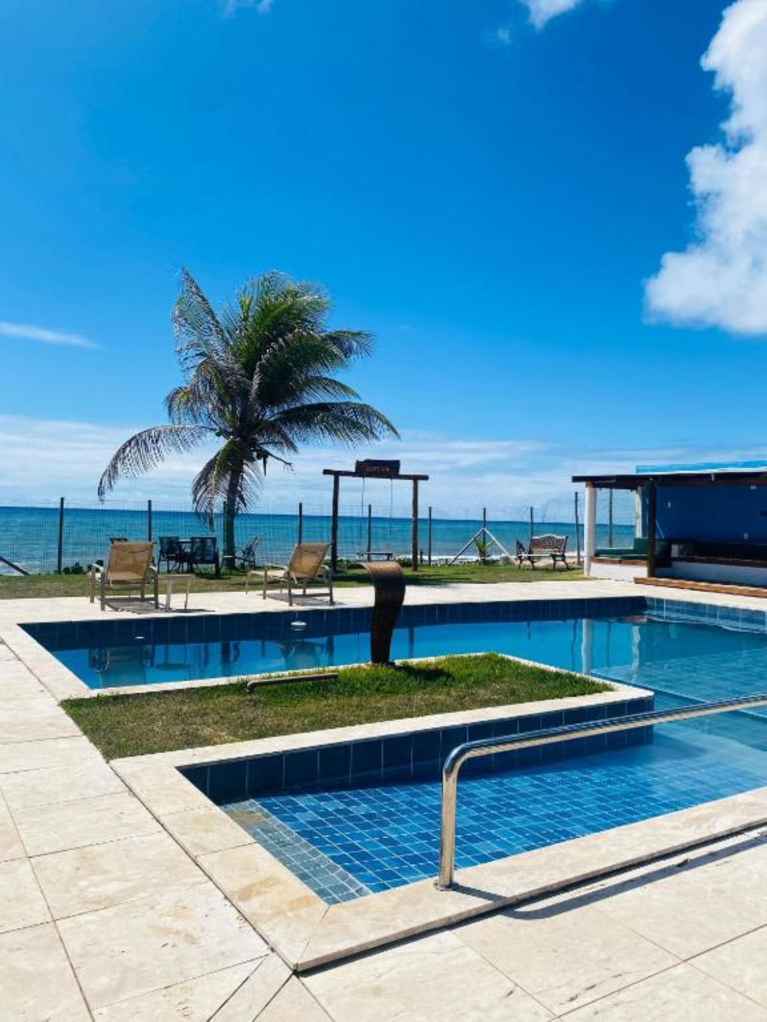 A swimming pool with lounge chairs and a palm tree, overlooking a clear blue sky and ocean.