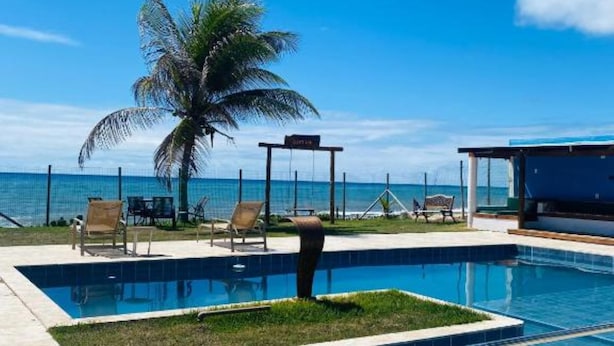 A swimming pool with lounge chairs and a palm tree, overlooking a clear blue sky and ocean. - Pousada destino  (Entre rios)
