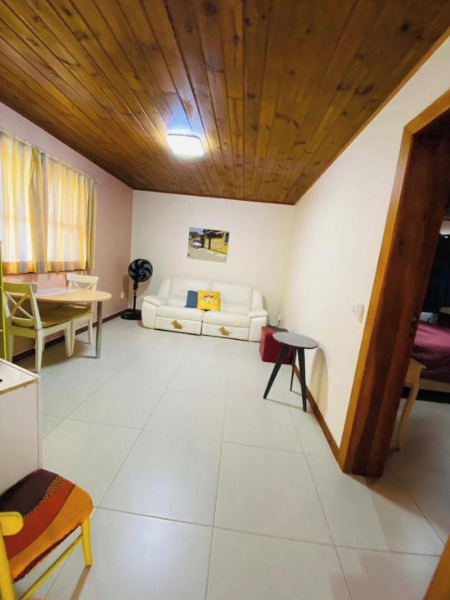 Una habitación con techo de madera, un sofá blanco, una mesa de comedor con sillas y una mesita redonda.