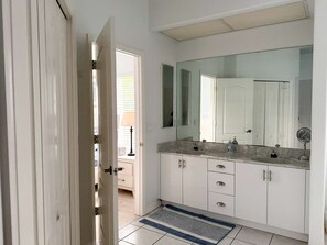 Un baño moderno con un espejo grande, armarios blancos y piso de baldosas.