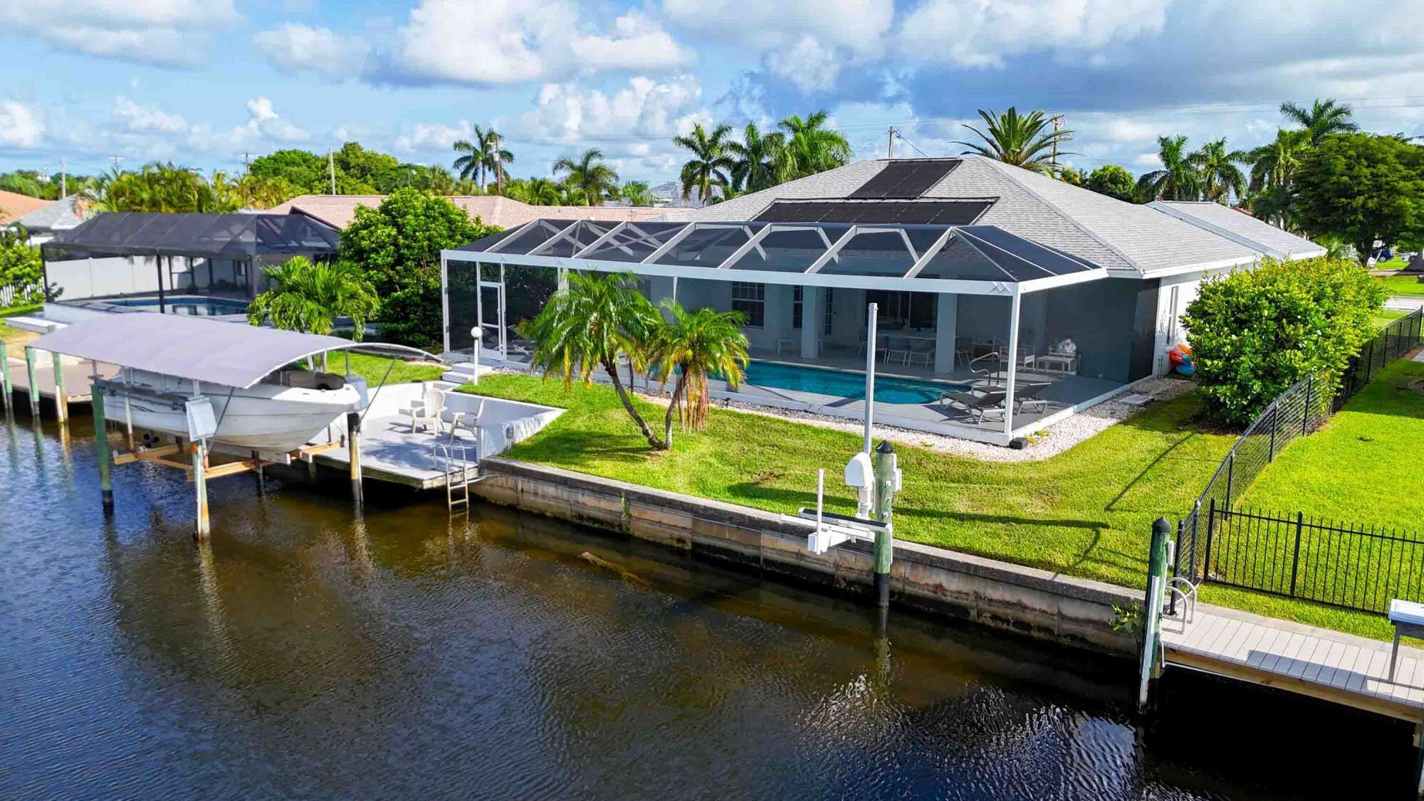 A modern house with a pool, a covered boat dock, and a well-maintained lawn.