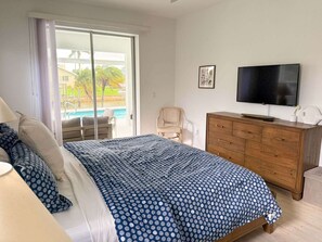 A bedroom with a bed, a wooden dresser, a television, and a view of a pool. - Villa Dolphin – Prime Location, Southern Exposure, Pool & Gulf Access (Cape Coral)
