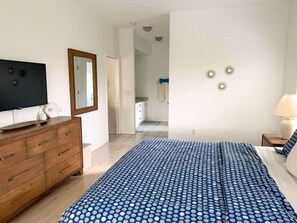 Un dormitorio con cama, cómoda, televisor y un pasillo que conduce a un baño.