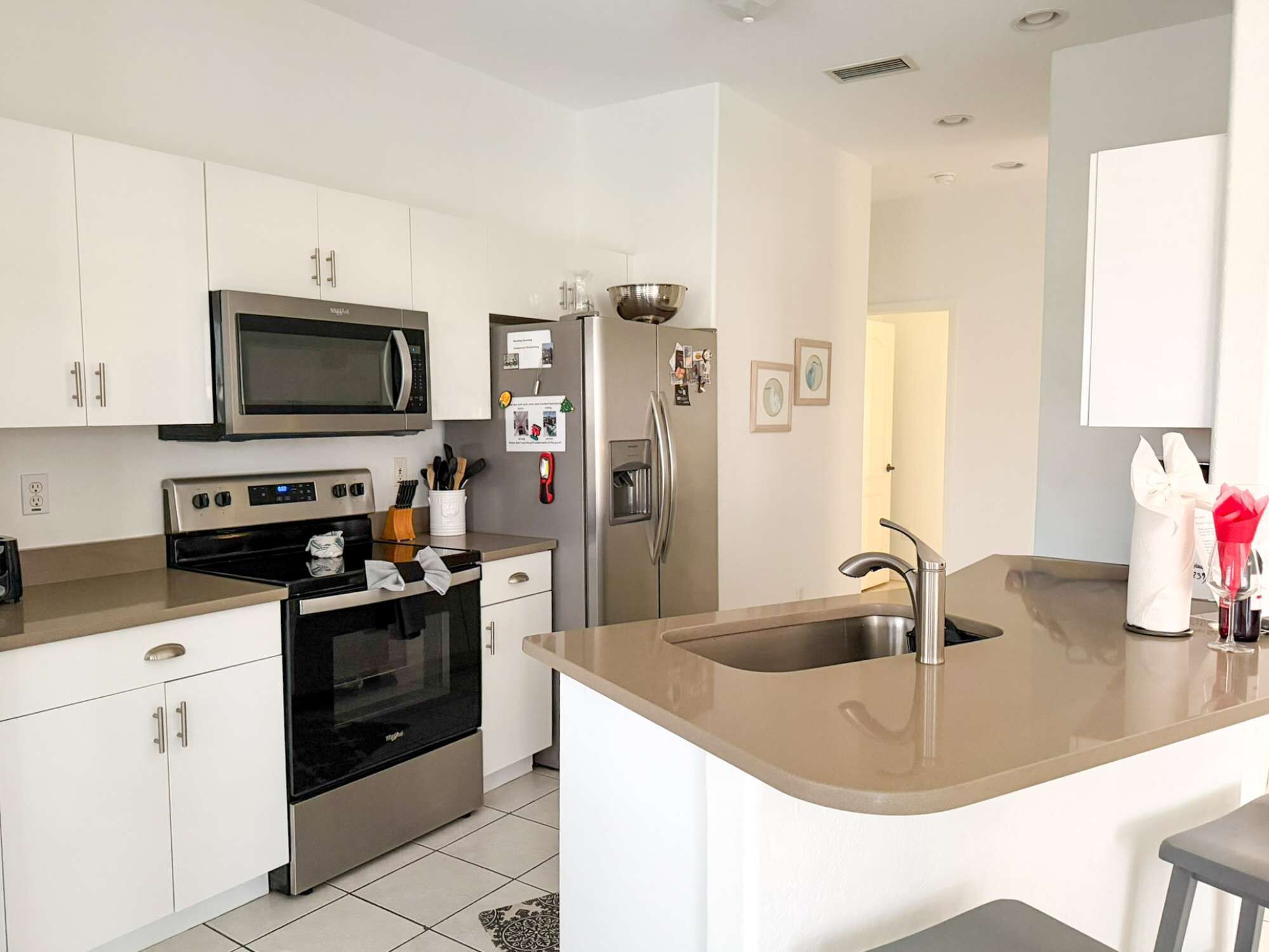 Una cocina moderna con armarios blancos, un refrigerador de acero inoxidable, un microondas, un horno y un lavaplatos con un grifo contemporáneo.